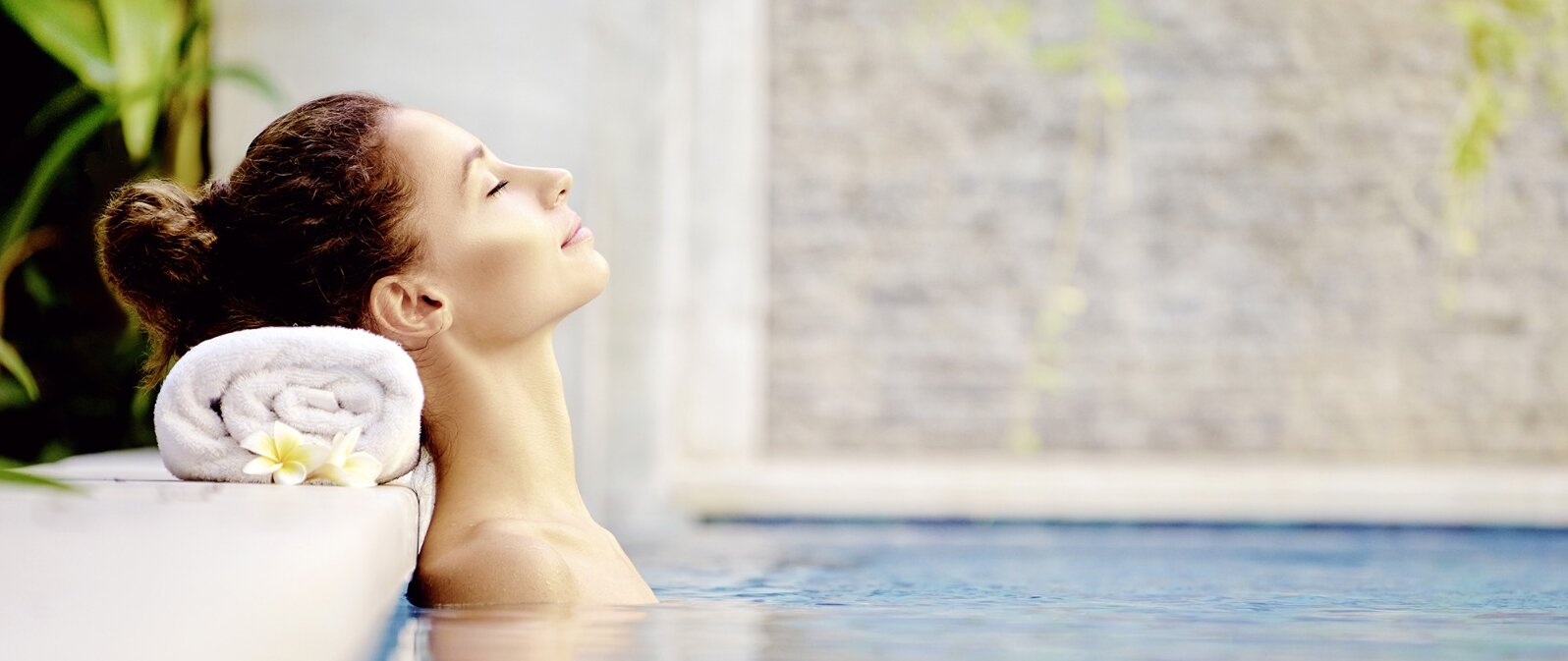 Frau entspannt sich im Pool, den Kopf auf einem aufgerollten Handtuch am Beckenrand