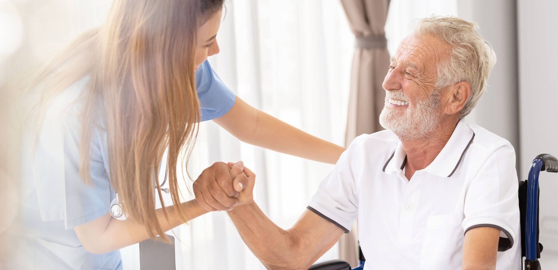 Krankenschwester und Patient im Rollstuhl geben sich erfreut die Hand.