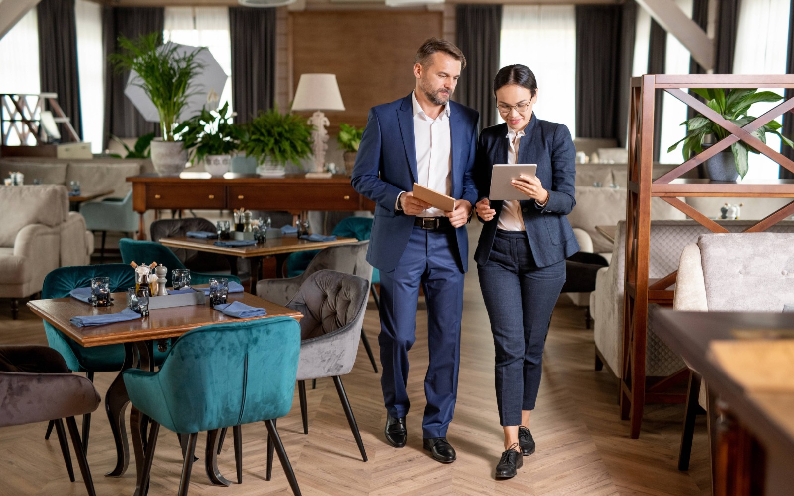 Ein Mann und eine Frau im Anzug stehen in einem modern eingerichtetem Restaurant und schauen auf einen kleinen Bildschirm